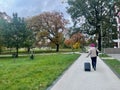 Woman with a suitcase is walking through the park. There's an airplane flying over her