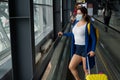 A woman with a suitcase is wearing a mask on the escalator at the airport.