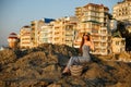 Woman with summer beach dress on sits on a rock and enjoys sun on vacation. Attractive beautiful girl with white straw Royalty Free Stock Photo