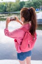 Woman in summer in city near lake, river pond, photographs landscape on smartphone, view from back, a pink backpack Royalty Free Stock Photo