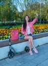 Woman in summer in a city park waves her hand, happy smiles rejoices, meeting and a date, scooter shop bag and bottle Royalty Free Stock Photo