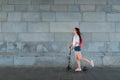 Woman in summer in city on scooter, rides motion. Backpack bag, white shirt pink backpack. Background wall transition by Royalty Free Stock Photo
