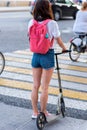 Woman in summer in city is waiting for a traffic light to cross road on a zebra crossing. Rear view, scooter shorts and