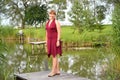 The woman in a summer claret dress stands on a planked footway near a pond Royalty Free Stock Photo