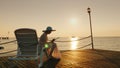 A woman in summer clothes sits on a lounger on the pier. Uses a tablet. A beautiful dawn on the sea, in the distance is Royalty Free Stock Photo