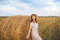Woman in a summer dress and straw hat poses on a haystack. Wheat field and blue sky at sunset Royalty Free Stock Photo