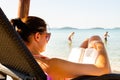 Woman on sun bed on the beach reading a book. People in background walking into sea Royalty Free Stock Photo