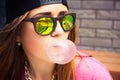 Woman in sunglasses and a cap makes a chewing gum bubble Royalty Free Stock Photo