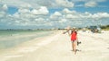 Woman in sunhat and red top walks on beach while using phone Royalty Free Stock Photo