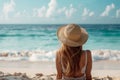 Woman in a sunhat relaxing on the sandy shore, gazing at the tranquil ocean