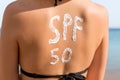 Woman with sunscreen in form of SPF 50 word on her back sunbathing at the beach. Sun protection factor concept Royalty Free Stock Photo