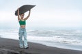 Woman surfer walking on black sandy beach, carrying white surfboard on head on background sea waves Royalty Free Stock Photo