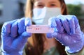 Woman with surgical mask holds coronavirus diagnostic test between latex gloves after successful test