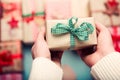 Woman surrounded by many wrapped christmas presents, holding beautifully wrapped tiny vintage present, point of view
