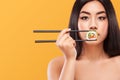 Closeup portrait of asian woman eating sushi and rolls on a yellow background. Copyspace.