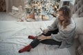 A woman in sweater sits on the bed and uses a smartphone. Christmas season