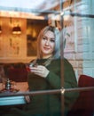 Woman in sweater sitting in restaurant with cup of fruit tea and looking out the window  view through glass Royalty Free Stock Photo