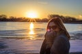 Woman in sweater standing on bridge by frozen lake at sunset Royalty Free Stock Photo