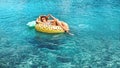 Woman swims on inflatable pineapple ring in the clear sea water.