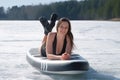 Woman in swimsuit basking in sun lying on sup board on frozen ice on river lake. Royalty Free Stock Photo