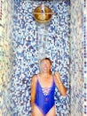 Woman in swimsuit standing under pouring ice water bucket in wellness area Royalty Free Stock Photo