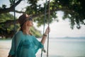 A woman is swinging on a swing in the shade of a big tree by the sea. Girl on the beach swing on the coast of a tropical Royalty Free Stock Photo