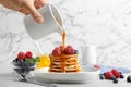 Woman syrup onto fresh pancakes with berries at light grey marble table, closeup