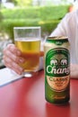 Woman holds glass of beer in her hands, next to it stands an aluminum beer can of the Thai brand Chang