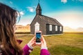 Woman take a photo by smartphone of Budir black church in Iceland