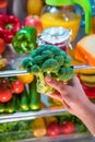 Woman takes the broccoli from the open refrigerator. Royalty Free Stock Photo