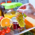 Woman takes the bunch of grapes from the open refrigerator Royalty Free Stock Photo