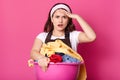 Woman takes in hands huge pink basin with dirty clothes, blankets, towels and other home textile, prepares for washing, has