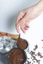 A woman takes a spoonful of ground coffee from a coffee grinder and puts it in a geyser coffee machine.