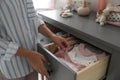 Woman taking baby clothes from open cabinet drawer in child room