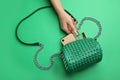 Woman taking bottle of perfume from small bag on green background, top view