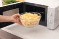 Woman taking bowl of popcorn from microwave oven in kitchen