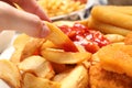 Woman taking delicious baked potato wedge with ketchup at table, closeup