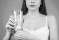 Woman taking drugs to releave headache. Brunette take some pills, holds glass of water, isolated on blue. Black and