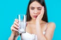 Woman taking drugs to releave headache. Brunette take some pills, holds glass of water, isolated on blue. Young woman Royalty Free Stock Photo