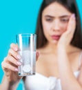 Woman taking drugs to releave headache. Brunette take some pills, holds glass of water, isolated on blue. Young woman