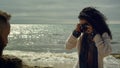 Woman taking family photos by ocean waves beach. Curly hair girl using camera.