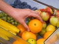 Woman taking orange from fridge drawer full of fruits