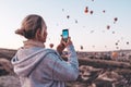 Woman taking photo on beautiful landscape and balloons in Cappadocia with mobile camera, sunrise time