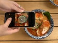 Woman taking photo of bowl of Tom Yum Kung noodle on her smartphone to share on social networks