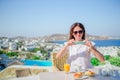 Woman taking photo of breakfast using her phone with amazing view of Mykonos. Girl taking pictures of food on luxury