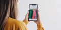 Woman taking a photo of colorful clothes on hangers with a smartphone. She is wearing a mustard yellow top, and the