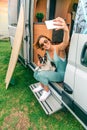 Woman taking photo sitting with her dog at door of camper van