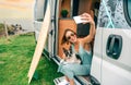 Woman taking photo sitting with her dog at door of camper van