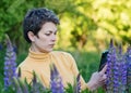 Woman taking photos of purple Lupines on the phone on the green grass at sunset Royalty Free Stock Photo