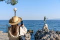 Woman taking photos of a Statue of a maiden with seagull on rocky coast in Opatija, Croatia. Royalty Free Stock Photo